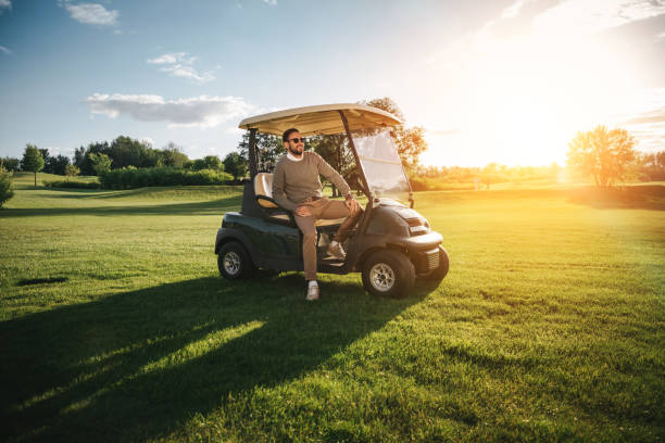 handsome bearded man in sunglasses sitting in golf car and looking away - golf course golf people sitting imagens e fotografias de stock