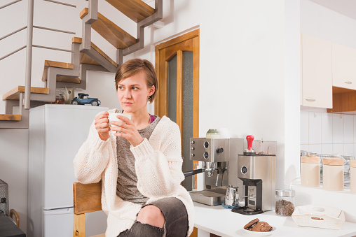 Portrait of pretty young woman sipping coffee from white cup of coffee at home early in the morning in a casual setup