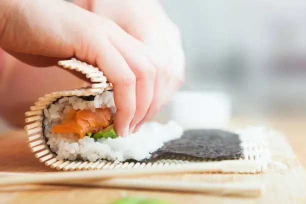 Photo of Preparing, rolling sushi. Salmon, avocado, rice and chopsticks on wooden table.