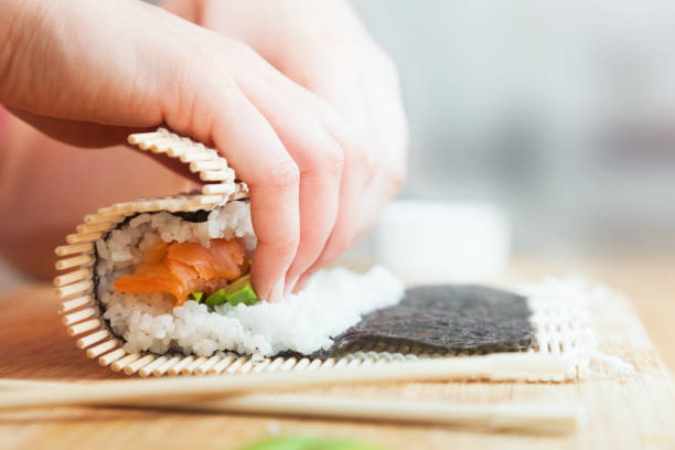 preparing, rolling sushi. salmon, avocado, rice and chopsticks on wooden table. - sushi japan maki sushi salmon imagens e fotografias de stock