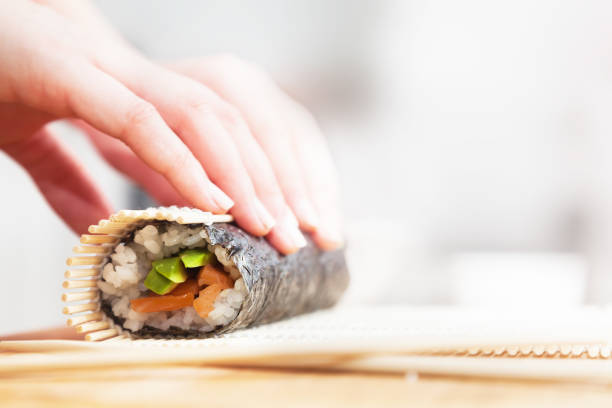 istock Preparing, rolling sushi. Salmon, avocado, rice and chopsticks on wooden table. 804432146
