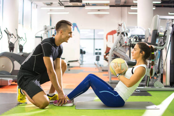 Female client doing abdominal crunches with ball while her personal trainer assisting her. Female client doing abdominal crunches with ball while her personal trainer assisting her. drive ball sports photos stock pictures, royalty-free photos & images