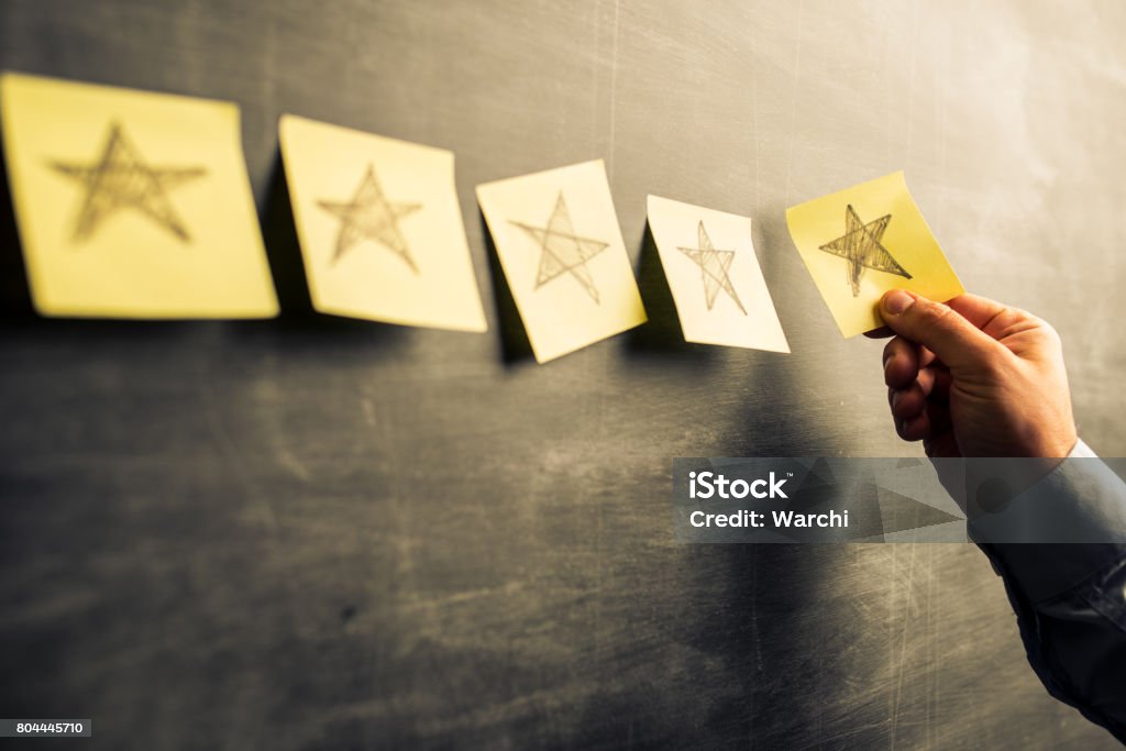 Five stars rating businessman attaching yellow  notes on blackboard with hand drawn stars Performance Stock Photo