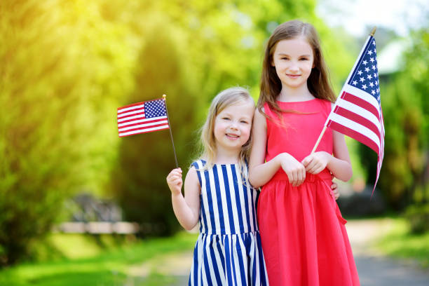 due adorabili sorelline che tengono bandiere americane all'aperto nella bellissima giornata estiva - youth culture foto e immagini stock