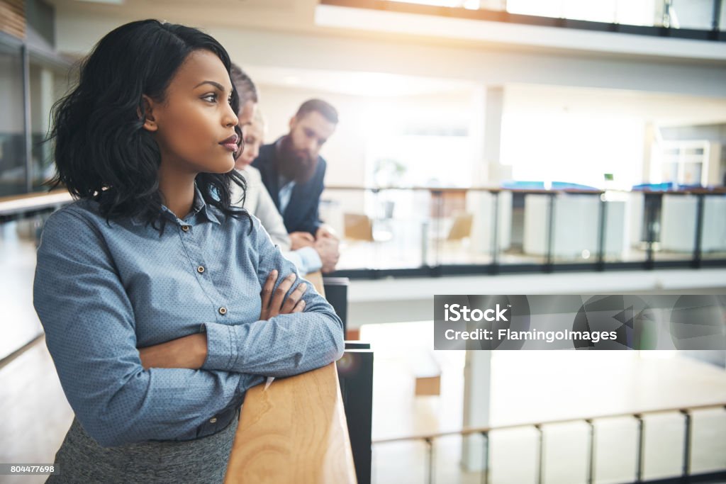 Pretty black woman in office looking away and thinking Attractive young African-American businesswoman standing in office with arms crossed and looking away thoughtfully. Contemplation Stock Photo