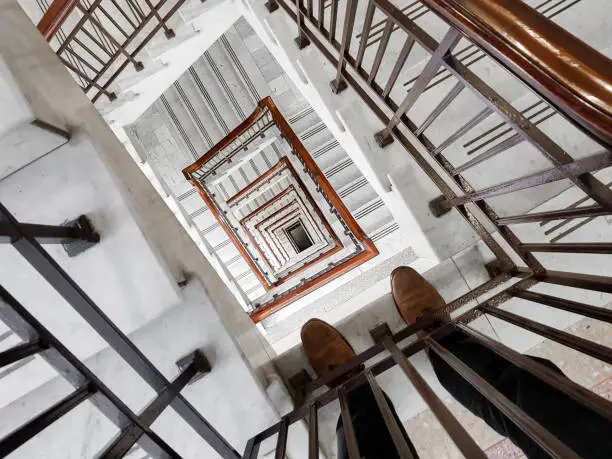 Perspective of young man looking over hand rail and down at interior spiral staircase descending through many levels