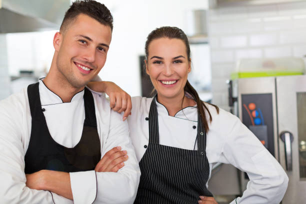 два улыбающихся повара на кухне - hat women chef occupation стоковые фото и изображения