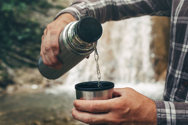 istock Unrecognizable Traveler Pouring Tea Or Coffee To Cup From Thermos On Waterfall Background. Tourism And Travel Concept 804495844