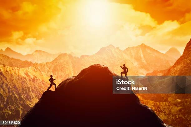 Two Men Running Race To The Top Of The Mountain Competition Rivals Challenge Stock Photo - Download Image Now