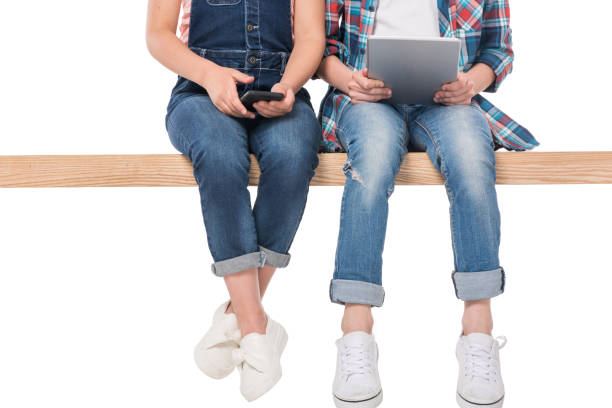 istock low section of boy and girl using digital devices while sitting on bench, isolated on white 804554496