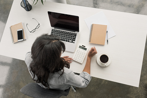 overhead view of young businesswoman using calculator on workplace at office