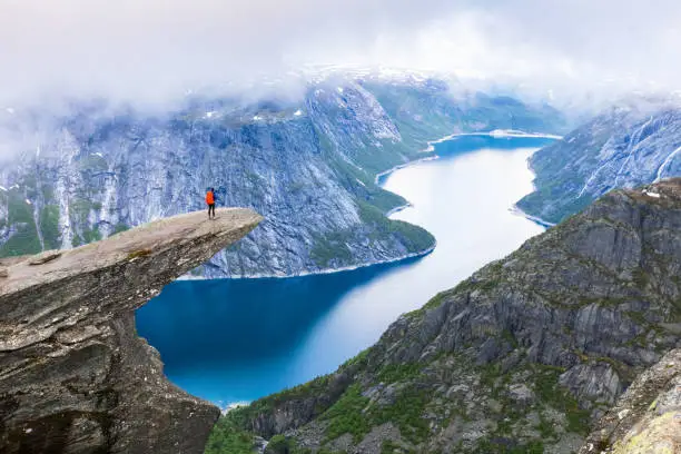 Photo of Hiker standing on Trolltunga with panoramic view of lake, Norway