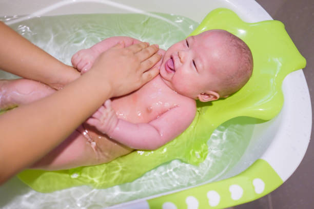 Happy four months old asian smiling baby taking a bath. Smiling kid in bathroom with mother stock photo