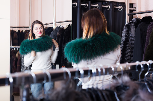 Pretty woman customer examining new fur neckpiece in womenâs cloths store