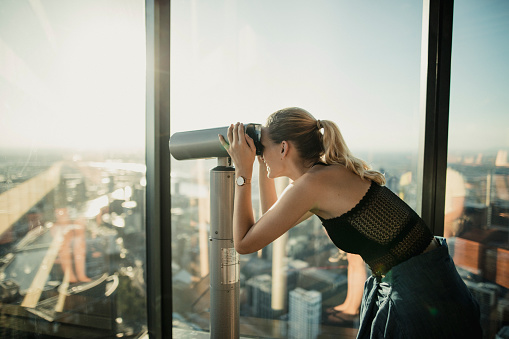 Young woman looking through binoculars at the Eureka Skydeck in Melbourne, Australia.