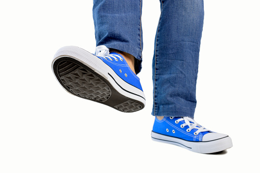 close up of steps of a person with sneakers and jeans walking isolated white background