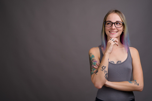 Studio shot of young beautiful woman with multi colored hair and tattoos wearing gray tank top against gray background horizontal shot