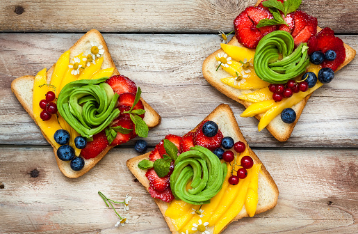 Sandwich with avocado,fruits and berries over rustic wooden background. Raw food. Healthy food for breakfast or lunch.