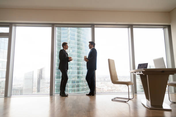 istock Two businessmen standing at full-length window in office, coffee break 804671322