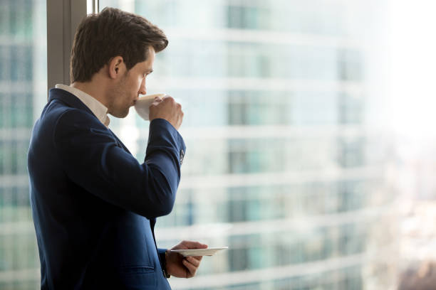 istock Thoughtful businessman drinking coffee, looking through office window at city 804671330