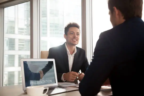 Photo of Smiling investment broker showing presentation on laptop screen to client