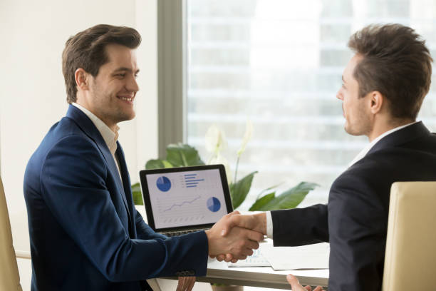 Two smiling businessmen handshaking, partners satisfied with financial growth data