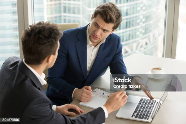 Two Serious Businessmen Using Laptop Discussing New Project At Office Stock Photo - Download Image Now