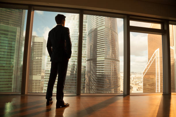 hombre de negocios reflexivo fuera de ventana grande en la puesta del sol ciudad - full length windows fotografías e imágenes de stock