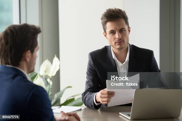 Distrustful Businessman Holding Document Reading Bad Resume At Job Interview Stock Photo - Download Image Now