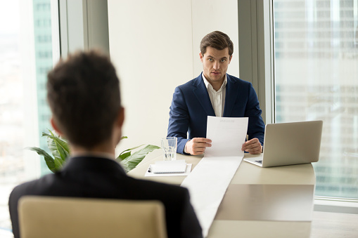 Surprised employer holding long sheet of paper, detailed resume of applicant at interview, astonished recruiter amazed with impressive career achievements, client submitting huge list of complaints