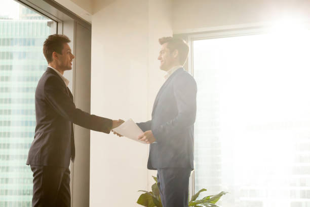istock Two smiling businessmen shaking hands while standing in sunny office 804671948