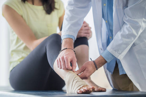 Foot Support A young Asian woman is getting bandage wrapped around her foot by a male doctor inside a doctor's office. She is in a session for physical therapy. orthopedics stock pictures, royalty-free photos & images