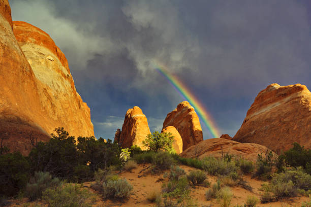 istock Rainbow bursts from clouds as sun lights red rocks 804705904