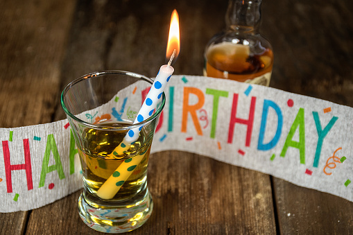 whiskey and candle in shot glass with birthday banner and bottle on rustic wood