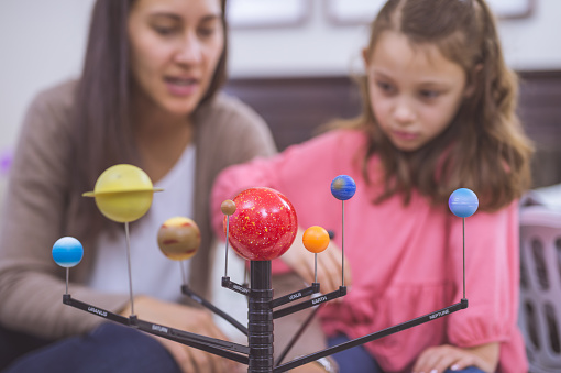 Mother and Daughter learning about astronomy together with model of planets on bed