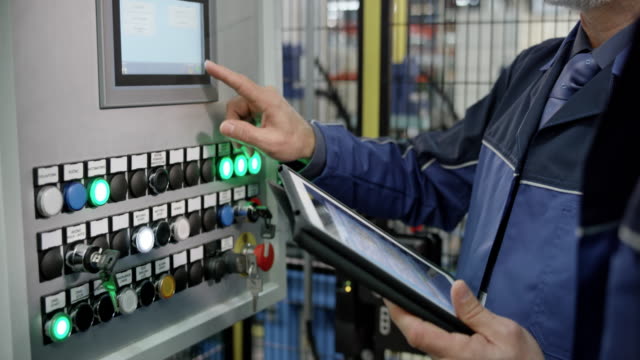 Male employee entering data using a touch screen on the machine in the factory