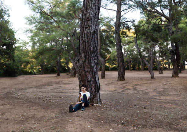 istock Young woman sitting under the tree and surf on the internet 804811810