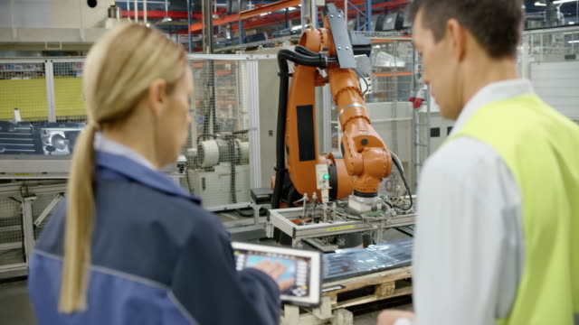 Female engineer and representative of the company manufacturing robots inspecting the performance of the industrial robots
