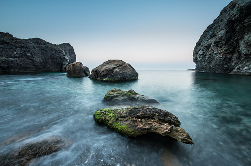 Stones in the sea on a long exposure. Scenic sunrise on a rocky seashore.