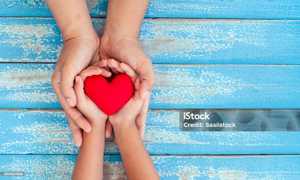 Cuore rosso in bambino e madre mani su vecchio tavolo di legno blu - Foto stock royalty-free di Bambino