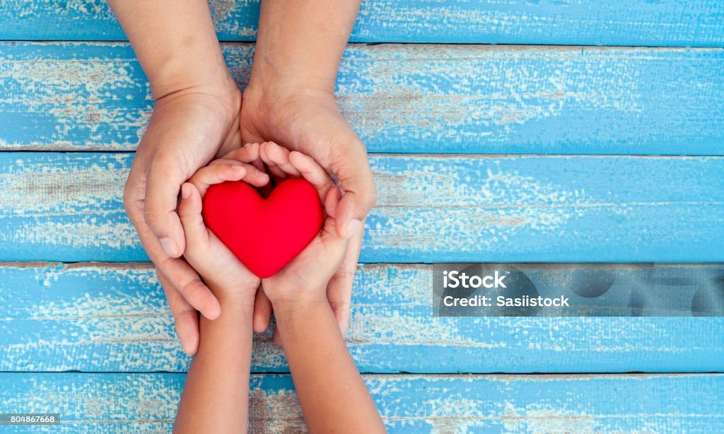 Red heart in child kid and mother hands on old blue wooden table Red heart in child kid and mother hands on old blue wooden table in vintage retro style Child Stock Photo