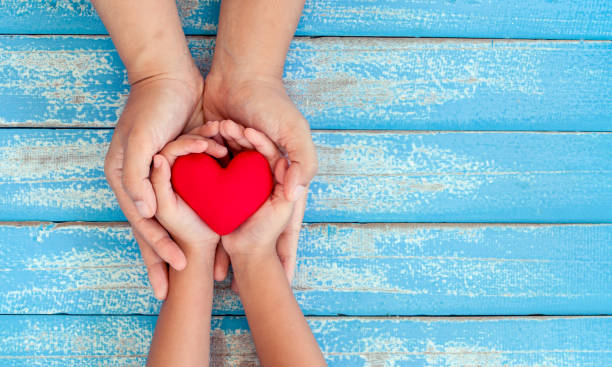 Red heart in child kid and mother hands on old blue wooden table stock photo