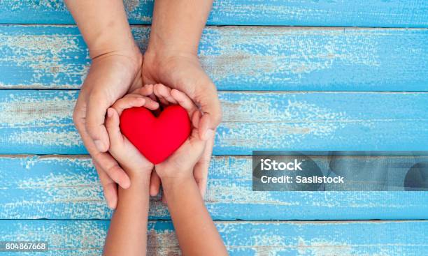 Red Heart In Child Kid And Mother Hands On Old Blue Wooden Table Stock Photo - Download Image Now