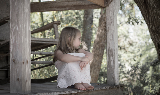 Portrait of a 4 year old girl sitting on a porch deep in thought.