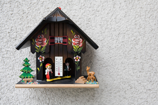 Stock photo showing a beautiful Christmas village display, which features numerous illuminated houses. The houses have been placed on artificial grass and sprinkled with fake snow to create a snowy scene, on top of a chest of drawers, complete with a forest of plastic spruce trees.