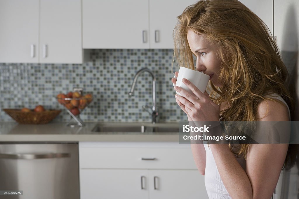 Красный голову женщина питьевой в kitchen - Стоковые фото В помещении роялти-фри