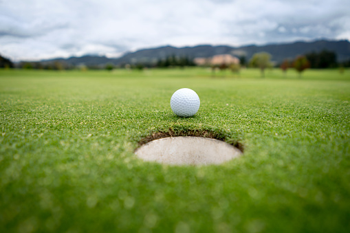 Close-up on a golf ball going into the hole in the putting green - sports concepts