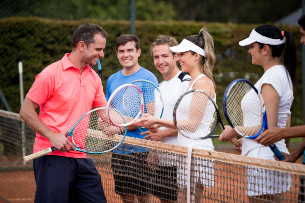 Coach giving a tennis lessons to a happy group of people Coach giving a tennis lessons to a happy group of people and smiling while showing them how to hold the racket - sports concepts tennis coach stock pictures, royalty-free photos & images