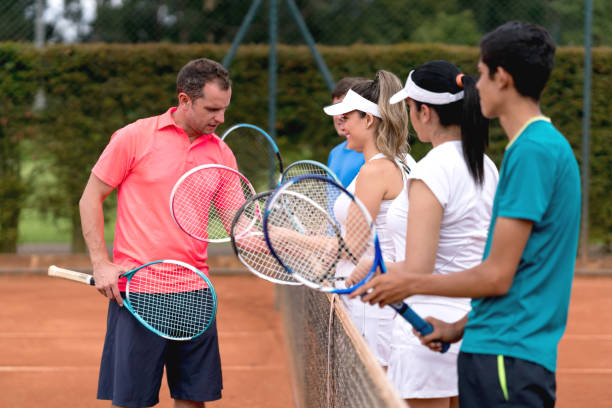 Coach teaching tennis lessons to a group of people Coach teaching tennis lessons to a group of people and helping them hold the racket properly - outdoors sports concepts tennis coach stock pictures, royalty-free photos & images