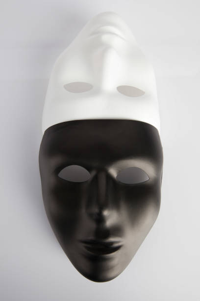 istock Black and white masks joined on white reflective background. Vertical image, top view. Anonymity concept. 804919880